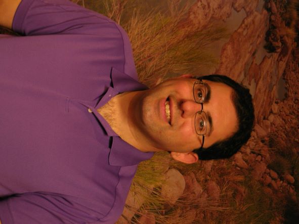 A man in purple shirt smiling for the camera.