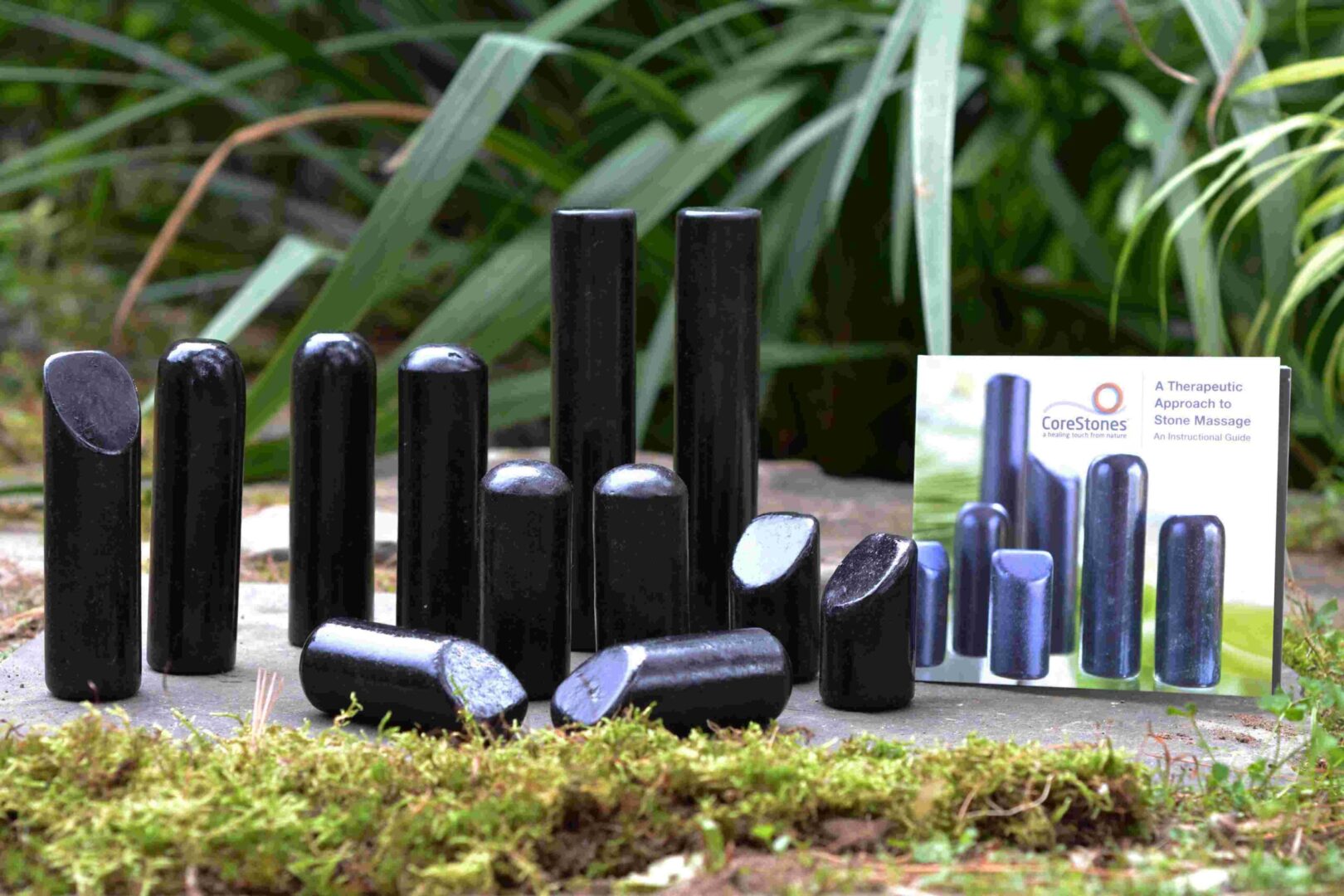 A group of black cylinders in a garden with moss around them.